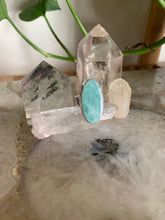 Load image into Gallery viewer, Oval Amazonite and sterling silver Ring on quartz crystal with crystal points and plant behind it. 